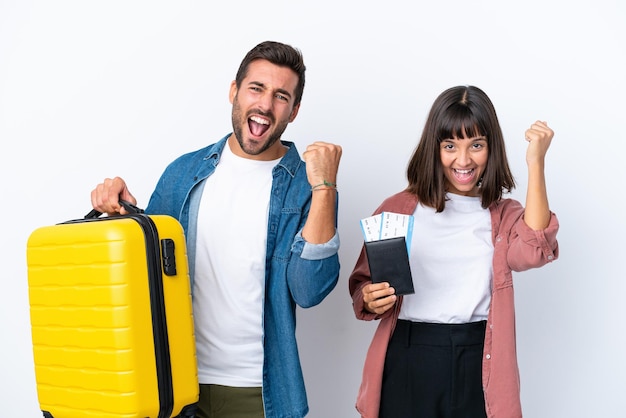 Casal jovem viajante segurando uma mala e passaporte isolado no fundo branco comemorando uma vitória