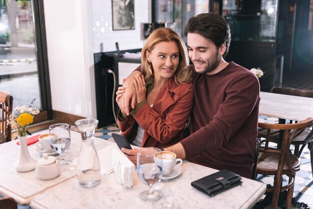 Casal jovial enérgico sentado em um restaurante e usando o telefone