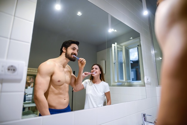 Foto casal lavando os dentes no banheiro.