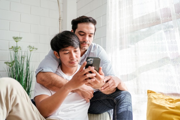 Foto casal lgbt caucasiano e asiático se abraçando de trás sentados e usando um smartphone juntos