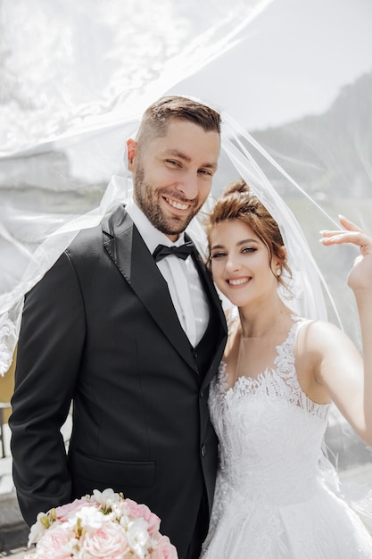 Casal lindo elegante sob véu Abraços um no outro Eles olham para a câmera e sorriem sinceramente