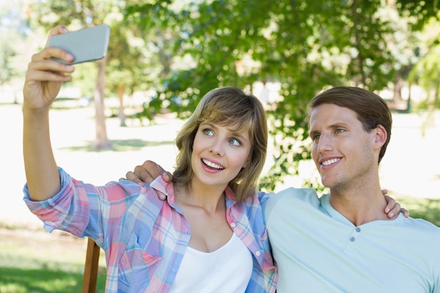 Casal lindo sentando-se no banco no parque tomando um selfie