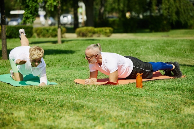 Casal maduro de ioga de manhã cedo, homem e mulher esportivos treinando ao ar livre no parque no verão quente