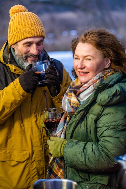 Casal maduro feliz desfrutando de vinho quente na aventura de acampamento de passeio romântico de inverno Alcance romântico de família de casal maduro com vinho quente perto de campista Aventura familiar e conceito de férias