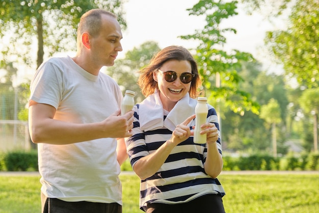 Casal maduro feliz no parque, descansando bebendo iogurte