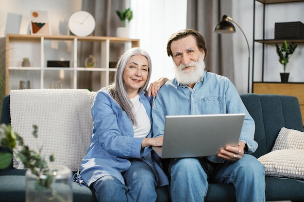 Casal maduro feliz usando laptop assistindo filme juntos sentado no sofá em casa