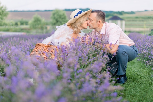 Casal maduro se beijando em roupas elegantes e elegantes, sentado em um lindo campo de flores de lavanda