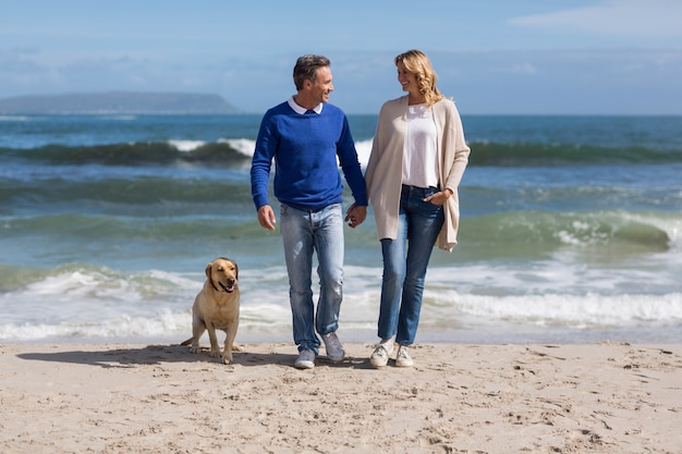 Casal maturo, caminhando na praia com seu cachorro