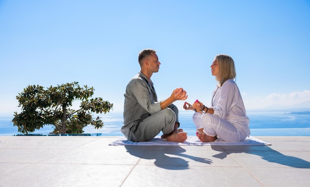 Casal meditando no terraço com bela vista para o mar