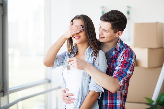 Foto casal mostrando as chaves para a nova casa se abraçando, juntos desempacotando caixas de papelão.