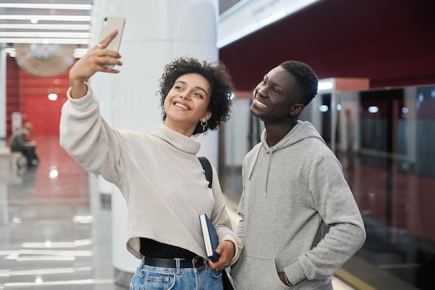 Casal multicultural tirando uma selfie em pé em uma plataforma de metrô