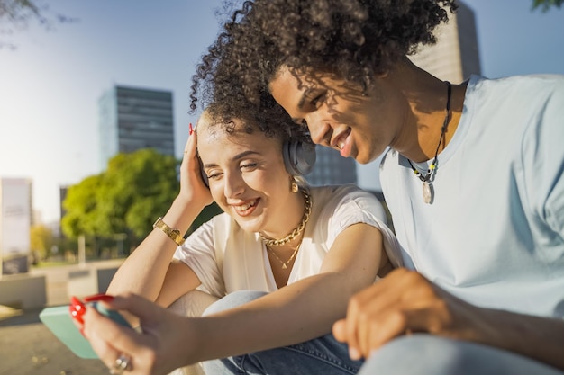 Casal multiétnico olhando o telefone ouvindo música e rindo na cidade Foto de alta qualidade