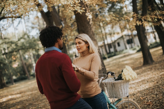 Casal multirracial com pé de bicicleta no parque outono