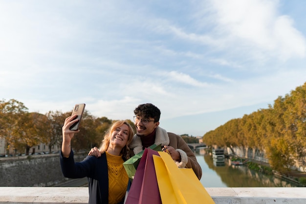 Casal multirracial de amigos tirando uma selfie muito feliz segurando sacolas de compras