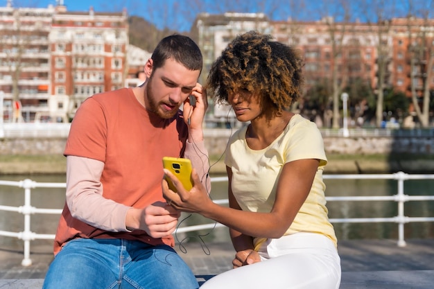 Casal multirracial nas ruas do estilo de vida da cidade sentado ouvindo música com fones de ouvido