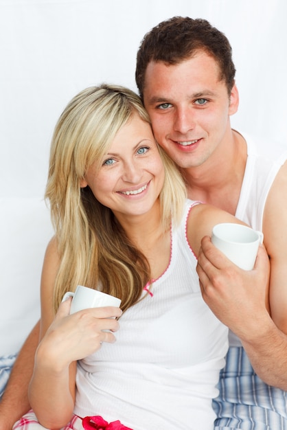 Foto casal na cama bebendo café e sorrindo para a câmera