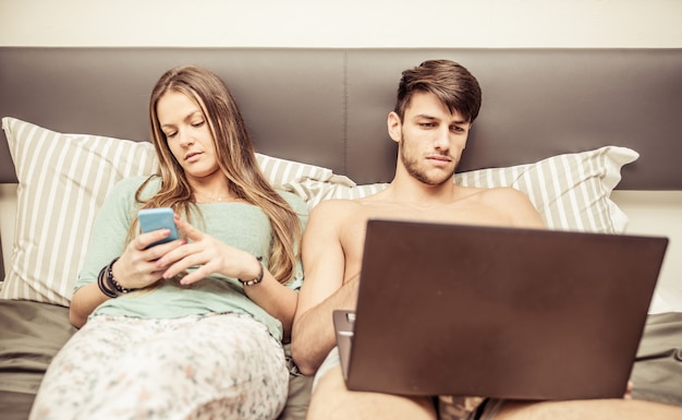 Casal na cama e tecnologia