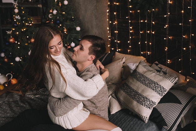 Casal na cama no quarto. Interior escuro. Ano Novo e Natal. Abraços e beijos. Ame. Suéter branco e meias altas. Encontro romântico. A amantes de data.