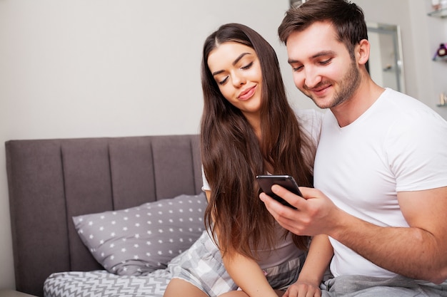 Casal na cama olhando para smartphone e sorrindo