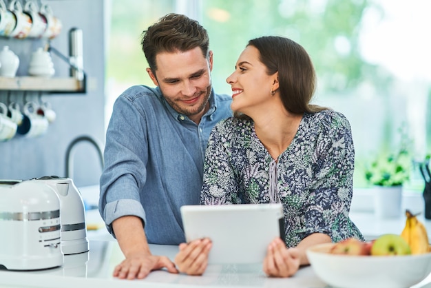 casal na cozinha de casa usando tablet eletrônico