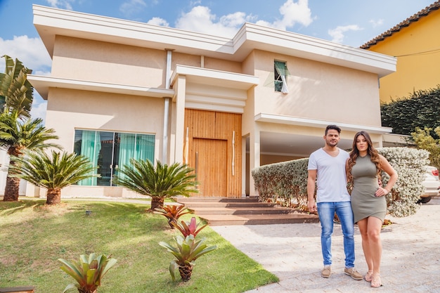 Foto casal na frente da nova casa grande e moderna, ao ar livre. casal feliz com a casa dos sonhos em segundo plano.