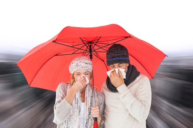 Casal na moda de inverno espirrando sob o guarda-chuva contra vista de alto ângulo da cidade