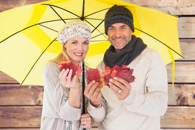 Casal na moda de inverno mostrando folhas de outono sob guarda-chuva contra fundo de pranchas de madeira