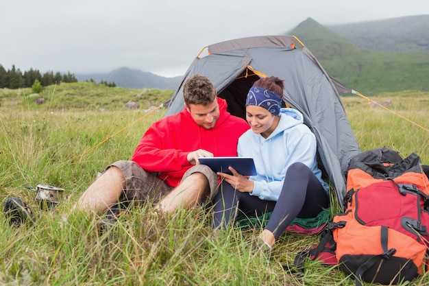 Casal na viagem de acampamento usando um tablet digital