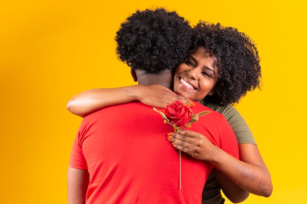 Casal negro abraçando em fundo amarelo e mulher segurando um botão de flor