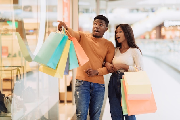 Casal negro animado com sacolas de compras apontando para a janela