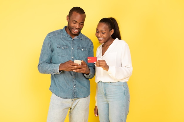 Casal negro fazendo compras usando telefone e cartão de crédito fundo amarelo