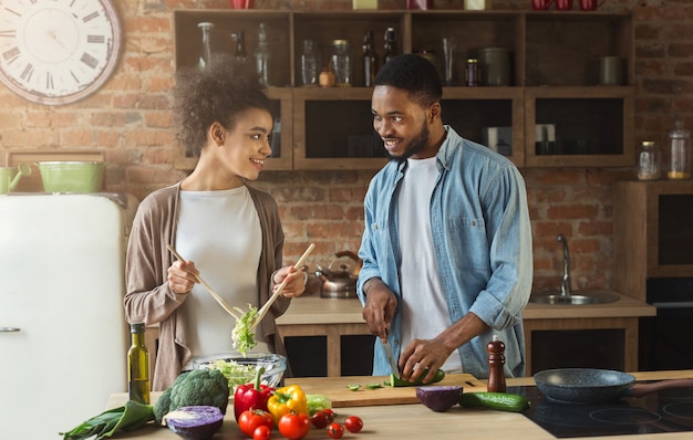 Casal negro feliz preparando salada saudável juntos na cozinha do sótão. Família jovem cozinhando o jantar