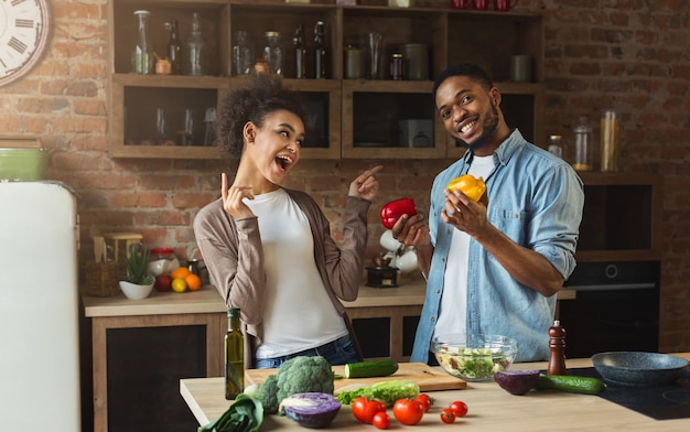 Casal negro feliz preparando um jantar saudável com pimenta no interior do loft