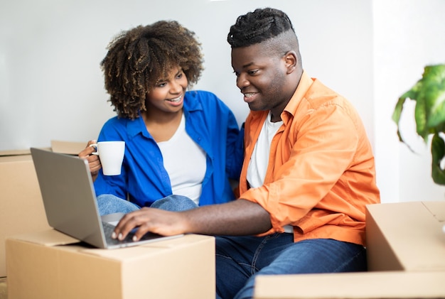 Casal negro feliz usando computador depois de se mudar para uma nova casa
