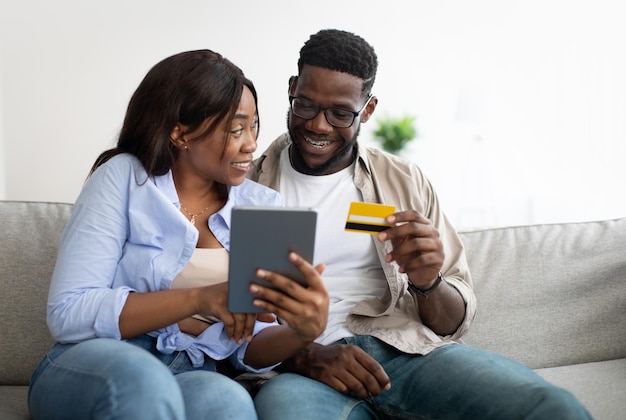 Casal negro usando tablet e cartão bancário em casa