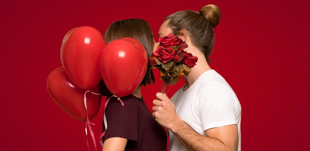 Casal no dia dos namorados com flores e balões com forma de coração sobre fundo vermelho