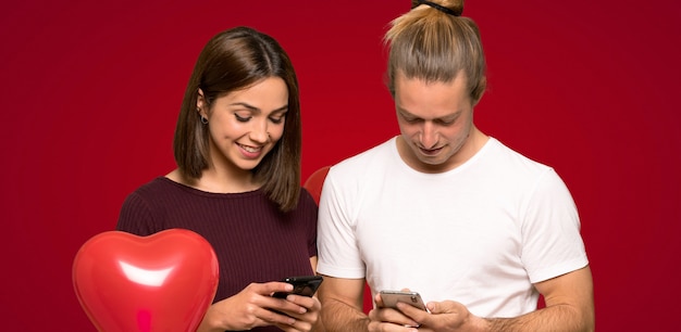 Casal no dia dos namorados, enviando uma mensagem com o celular sobre fundo vermelho