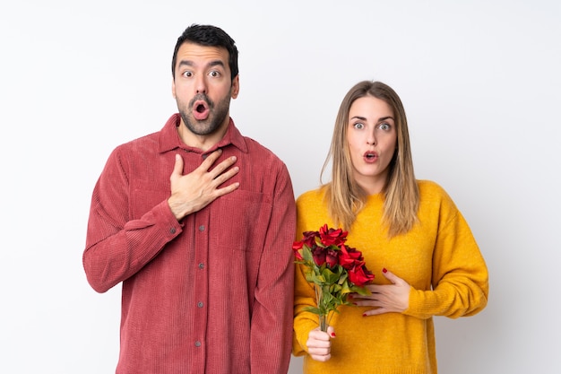 Casal no dia dos namorados, segurando flores sobre parede isolada com surpresa e expressão facial chocado