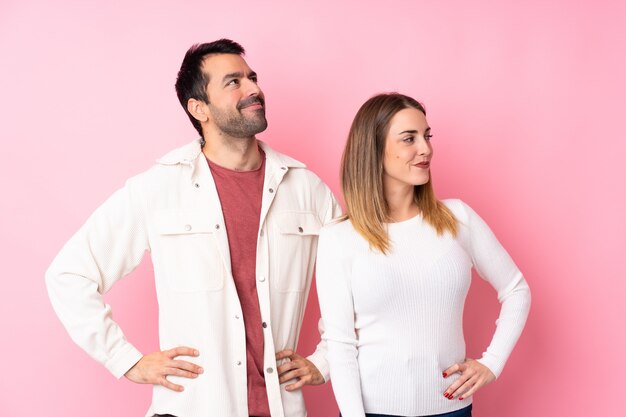 Casal no dia dos namorados sobre parede rosa isolada posando com os braços no quadril e rindo