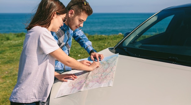 Foto casal olhando um mapa encostado no carro