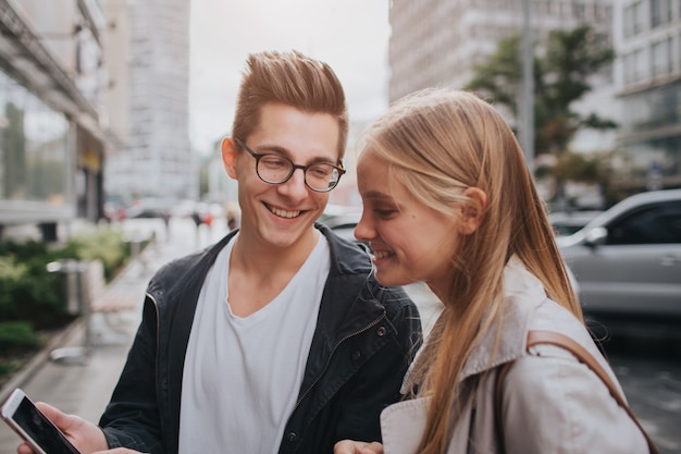 Casal ou amigos rindo engraçado e se divertindo com um telefone inteligente em uma rua da cidade grande.