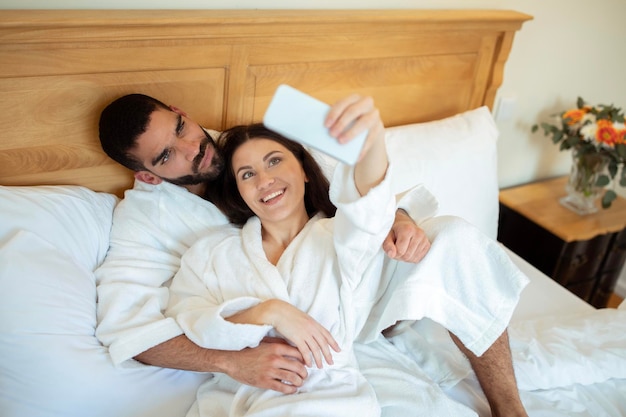 Casal posando para selfie usando telefone na cama no hotel