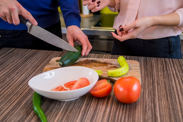 Casal preparando vegetais juntos em casa na cozinha. closeup de mãos humanas cozinhando salada de legumes na cozinha na mesa de madeira. comida saudável e conceito vegetariano