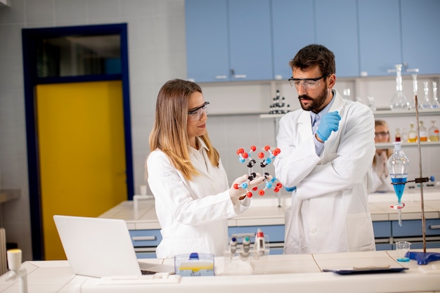 Casal químico com óculos de segurança mantém modelo molecular no laboratório