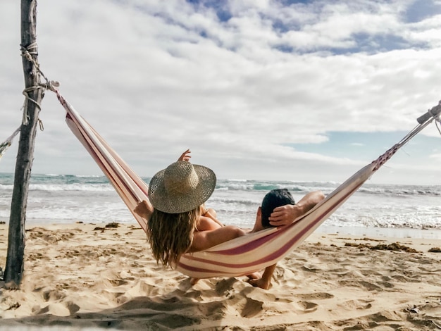 Foto casal relaxando em uma rede na praia contra o céu