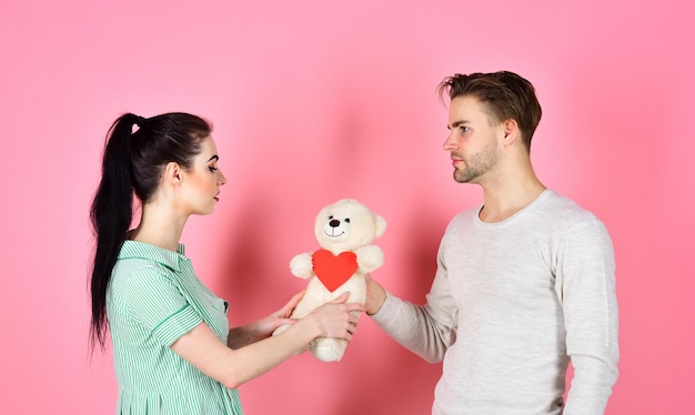 Casal romântico apaixonado Dia dos namorados e amor Conceito de presente bonito Homem bonito e linda garota apaixonada Casal de homem e mulher apaixonado segura cartões de dia dos namorados de coração e ursinho de pelúcia no fundo rosa