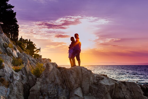 casal romântico dançando nas rochas à beira-mar no fundo do pôr do sol dramático roxo