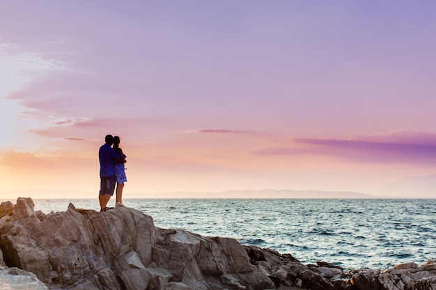 casal romântico dançando nas rochas à beira-mar no fundo do pôr do sol dramático roxo