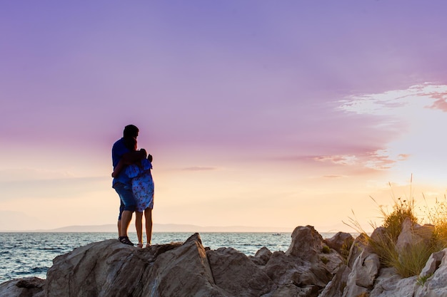 casal romântico dançando nas rochas à beira-mar no fundo do pôr do sol dramático roxo