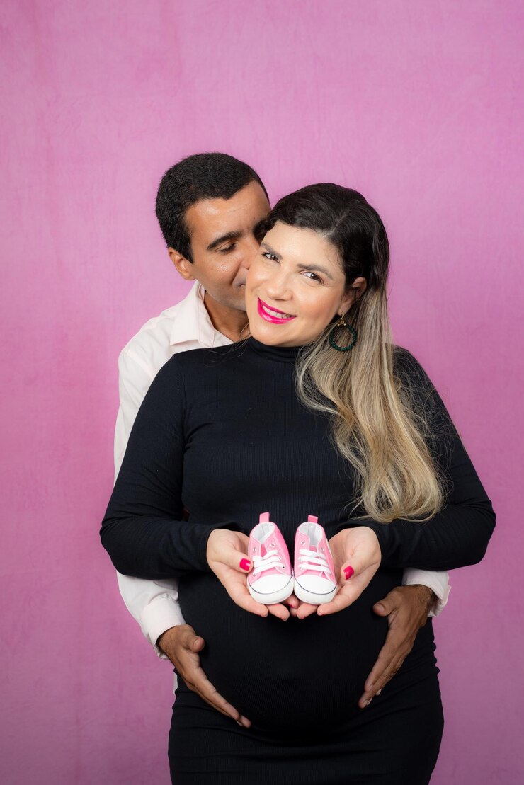 Foto casal romântico de marido bonito e linda esposa grávida posando no estúdio ela segura chinelos de bebê